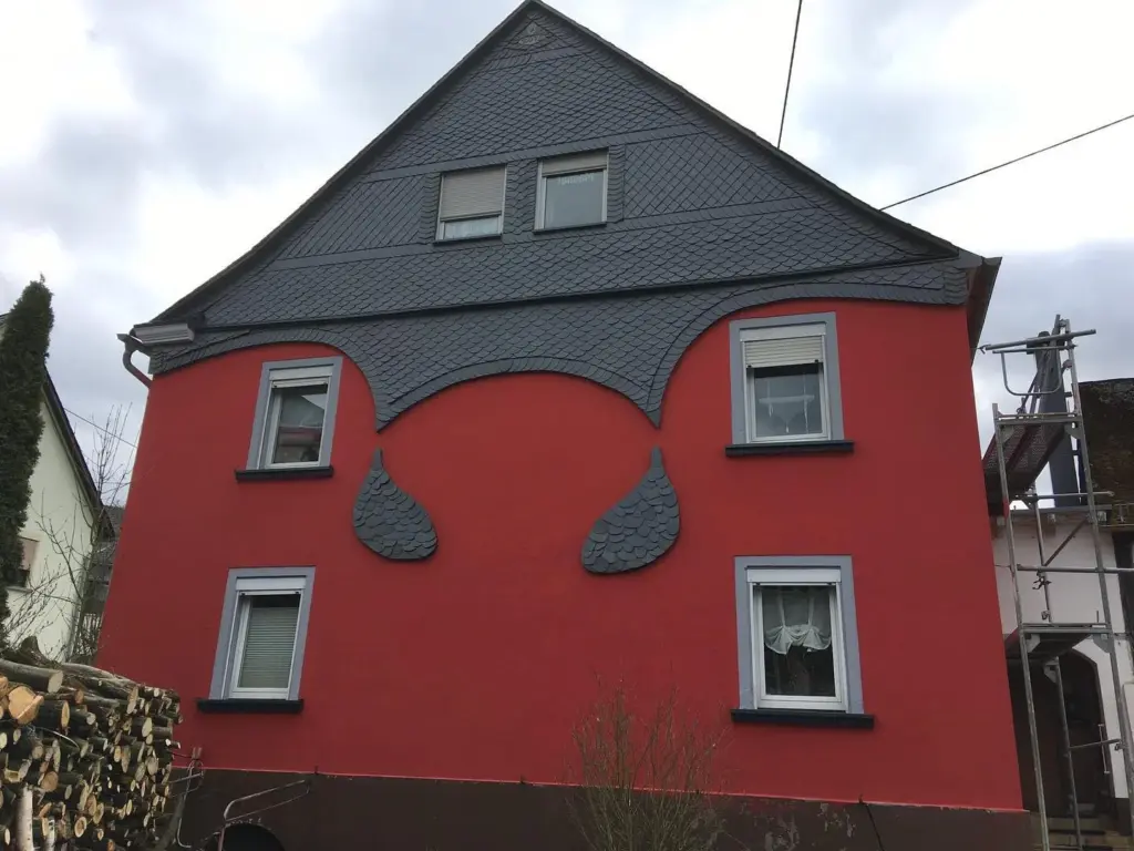 Giebel in Naturschiefer mit geschwungenen Schieferornamenten auf einer roten Putzfassade