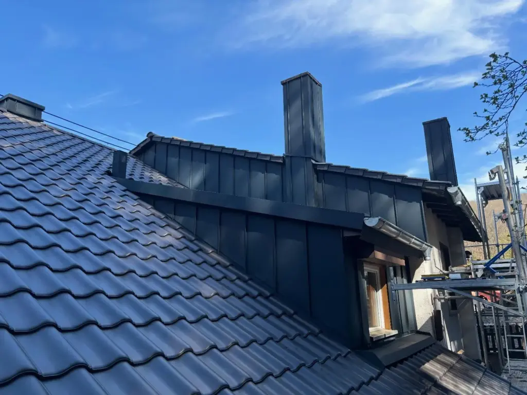 Gaubenwangen und Kaminverkleidungen in Winkelstehfalz aus anthrazitfarbenem Metall neben einem Ziegeldach