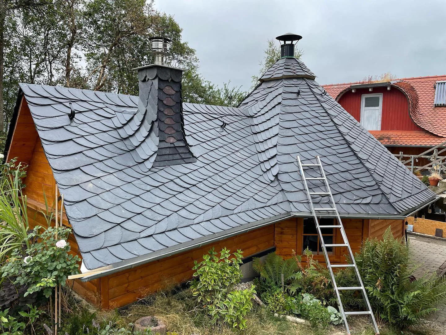 Naturschieferdach in Schuppendeckung auf einem Holzhaus mit schieferverkleidetem Schornstein, achteckigem Turmdach und eingebundener Kehle