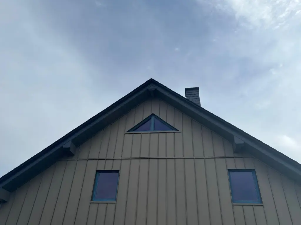 Giebelspitze einer PREFA-Stehfalzfassade in P.10 Bronze mit Dreiecksfenster und schieferverkleidetem Schornstein